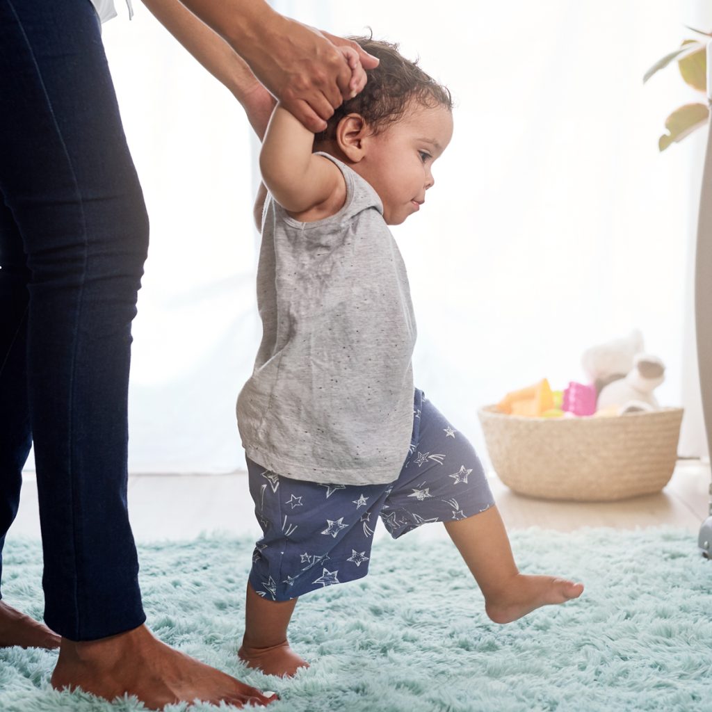 Baby holding nursery worker's hands and learning to walk independently