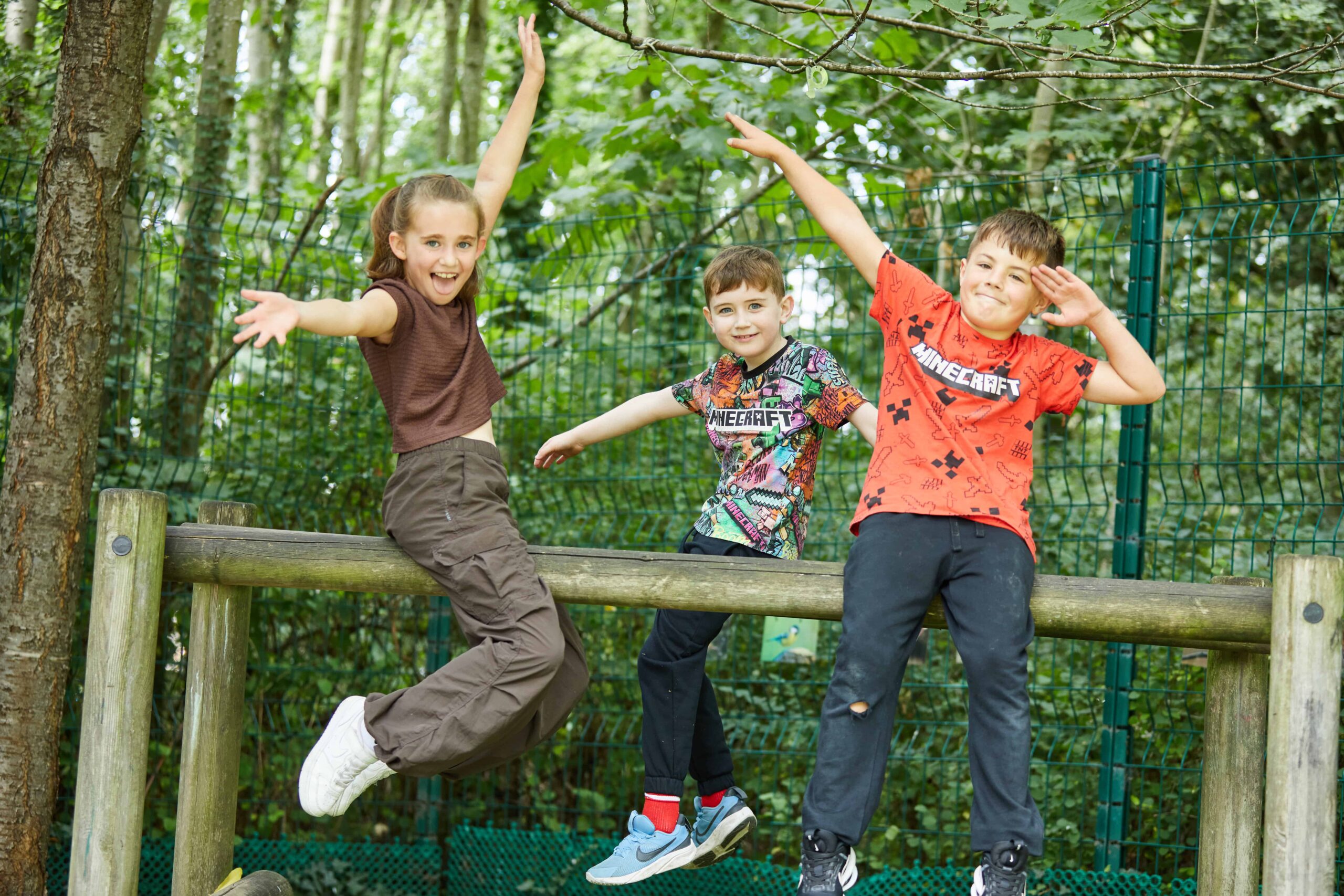 3 children sat on a wooden beam posing for a picture