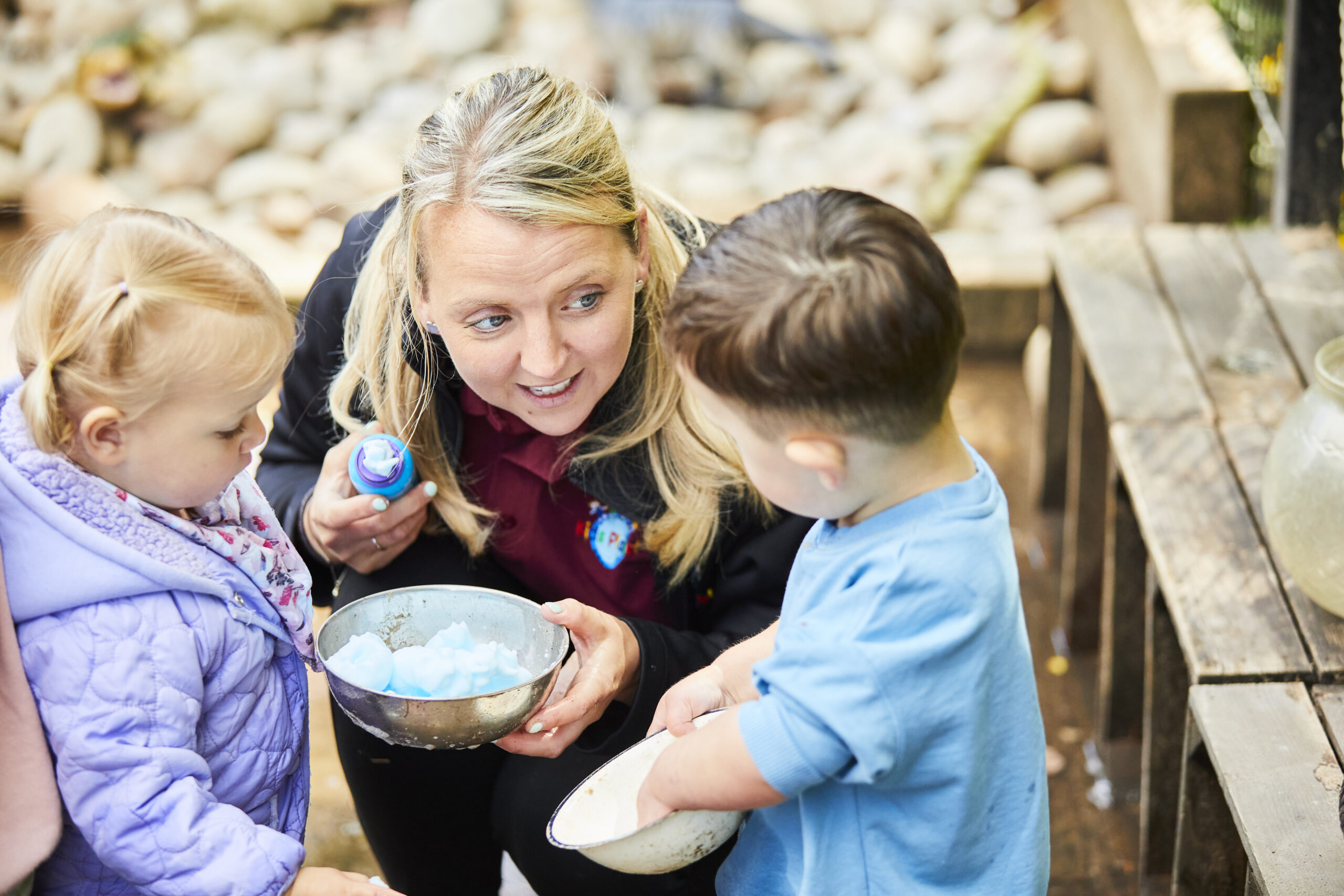a nursery staff member and 2 children interacting in the nursery garden