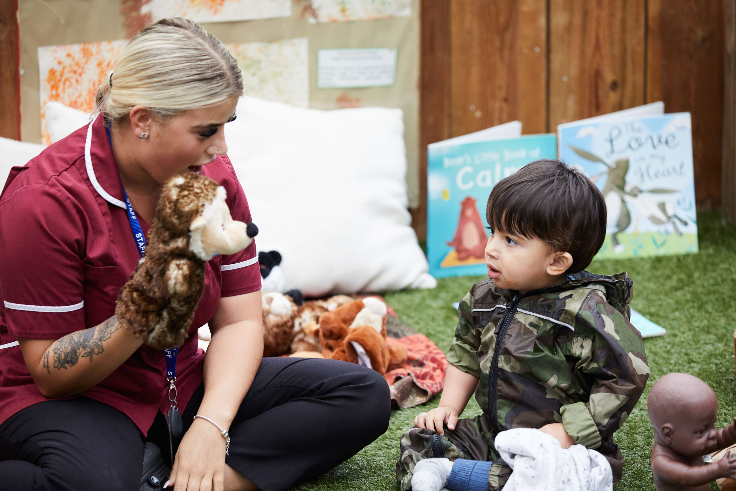 a nursery team member and a child playing in the nursery garden with puppets and books
