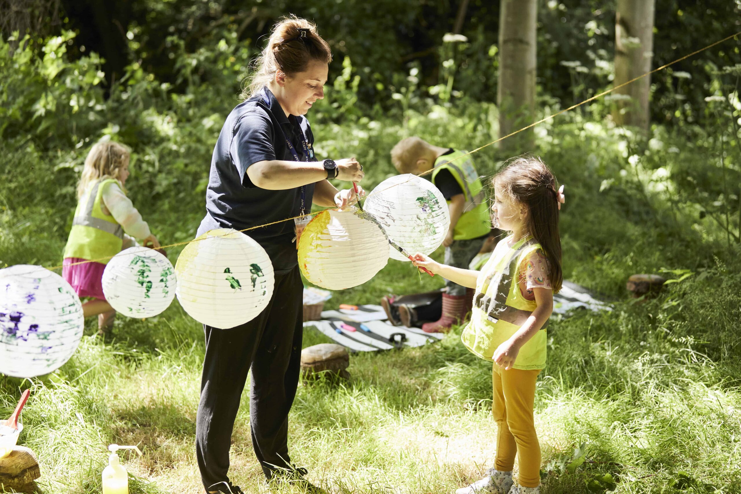image of a nursery team member and a child putting up some lanterns in the nursery garden