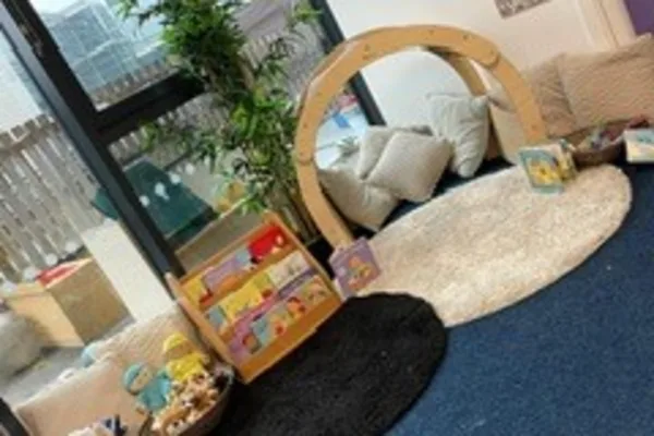 Wooden play arch frames pillows and a cream circular rug; low bookshelf displays colorful children's books, baskets of toys sit on an adjacent black rug near a window and plant.