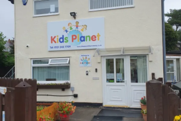 A colorful "Kids Planet" sign adorns the front of a converted house, marking a nursery entrance with double doors, a low fence, and potted flowers.
