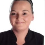 A head-and-shoulders portrait of a smiling adult facing the camera, hair pulled back, wearing a dark collared top against a plain white background.