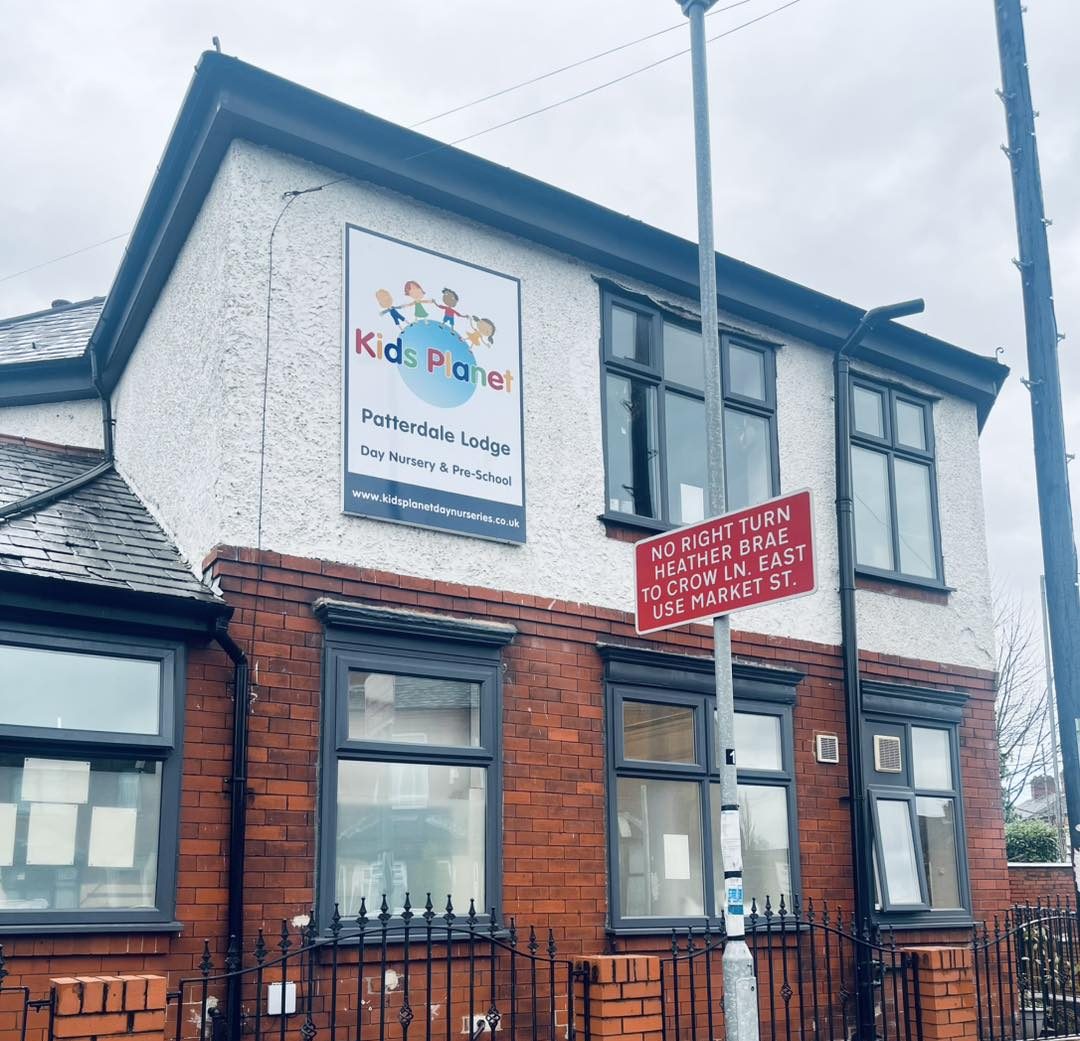 Kids Planet sign is mounted on a two‑storey brick-and-render building; a red traffic sign forbids a right turn on a lamppost; street-facing windows and an iron fence under an overcast sky.