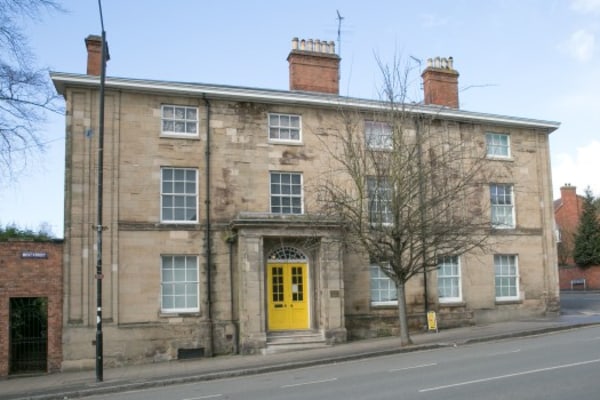 Three-story stone Georgian house stands facing a quiet street, featuring a bright yellow double front door, tall sash windows, chimneys, and a leafless tree on the pavement.