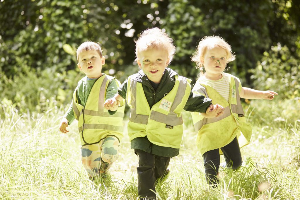 Three toddlers running through grass in the sunshine